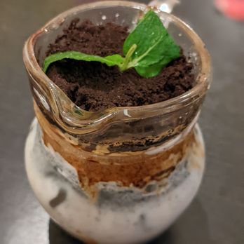 Unicorn Cafe - Black sesame potted plant - A layered dessert served in a glass jar, topped with cocoa powder and a mint leaf, placed on a dark surface. - Themed Cafes Near Me - Toronto, Ontario