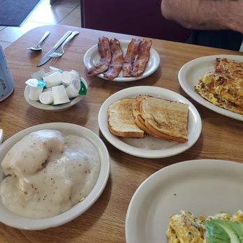 Cappy's Breakfast Cafe - So much good food - A breakfast spread with bacon, toasted bread, scrambled eggs, and biscuits with gravy on a wooden table, with utensils and creamers nearby. - Breakfast & Brunch Near Me - Tucson, Arizona