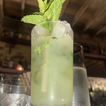 The Meadowlark - La Venenosa Tabernas Raícilla Takamine 8  Method Dry Vermouth Arak Alraah  Limpauras Green Matcha CordialLime Chartreuse Hibiki - A mojito cocktail with mint leaves garnishing the top, served in a tall glass with ice and lime slices, on a table. - Speakeasies Near Me - Chicago, Illinois