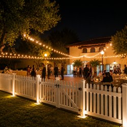 Elegant outdoor wedding reception with café lighting, white picket fencing, tables, chairs, and premium event rentals in Los Angeles.
