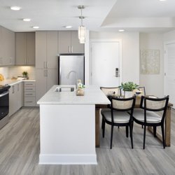 Camden Atlantic Apartments - Kitchen with modern latte color cabinetry, stainless steel appliances, quartz countertops, undermount sink, and glossy tile b...