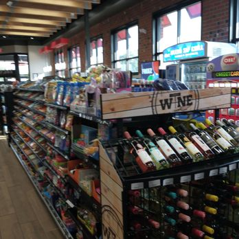 Sheetz - The image shows an aisle in a convenience store with shelves filled with snack foods, toys, and a wine display. The wine section features bottles arranged on racks, with a sign labeled 'WINE.' The store has large windows along the wall, allowing natural light to illuminate the interior. The ceiling has exposed wooden beams, and the floor is made of wood-like material. - Convenience Stores Near Me - Hilliard, Ohio