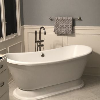 CAT Construction - Stand alone tub with new trim - A white freestanding bathtub is positioned against a wall with wainscoting, with a gray towel hanging on a towel bar above it. - General Contractors Near Me
