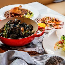 Mussels in a red pot served with French plates and glasses of white and rosé wine.