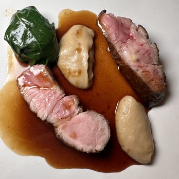 Margot - Pork Neck ($34) - A dish with sliced beef, a green leaf-wrapped item, and dollops of sauce on a white plate, served with a brown sauce. - New American Near Me - Brooklyn, New York