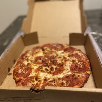 Pizza Leon - personal size pizza is really good and the perfect size for one person. - A pepperoni pizza with melted cheese and evenly distributed pepperoni slices is inside an open cardboard pizza box. The box is placed on a wooden surface, and the background is blurred. The pizza appears freshly baked with a golden crust and slightly browned cheese. - Pizza Near Me - Austin, Texas