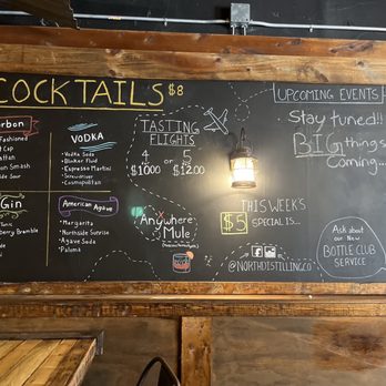 Northside Distilling - The image shows a black chalkboard mounted on a wooden frame at Northside Distilling. It lists various cocktails including bourbon, gin, vodka, and American agave, with prices and ingredients. Tasting flights are offered for $10 or $12, and a section highlights upcoming events and special offers, such as a $5 weekly special. The board also features illustrations, social media icons, and handwritten notes about the distillery's offerings and activities. - Distilleries Near Me - Cincinnati, Ohio