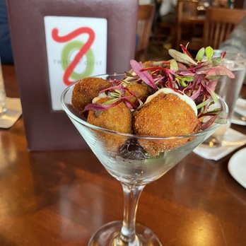 Twisted Olive - Twisted Olives - A martini glass contains fried appetizers topped with microgreens, set on a restaurant table with a menu and other diners in the background. - New American Near Me - Bethlehem, Pennsylvania