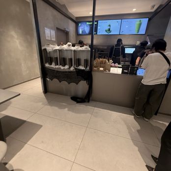 Hey Tea - A modern tea shop counter with digital menu screens displaying drink options, customers placing orders, and tea containers on a table. - Bubble Tea Near Me - Irvine, California