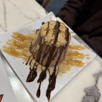 Vampire Penguin - Twix - A dessert featuring a chocolate and caramel sauce, topped with powdered sugar, presented on a white square plate with decorative drizzles. - Ice Cream & Frozen Yogurt Near Me - Brandon, Florida