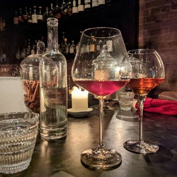 BarChef - Old world, and viceroy - Two wine glasses, one with rosé and one with amber wine, are placed on a dark bar table with a candle, water bottle, and cinnamon sticks nearby. - Lounges Near Me - Toronto, Ontario