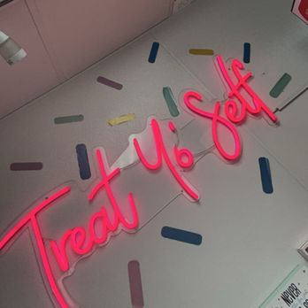 JJ's Custard Co - A neon sign with the phrase 'Treat Yo Self' in pink is mounted on a wall. The wall is decorated with various pastel-colored sprinkle shapes, creating a playful and inviting atmosphere. The sign is illuminated, making it stand out against the background. - Ice Cream & Frozen Yogurt Near Me - Dearborn, Michigan