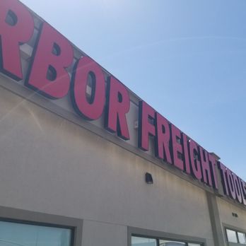 Harbor Freight Tools - Tool hunting - Photo shows the exterior of a Harbor Freight Tools store with a large sign displaying the store name in pink and purple letters. The building has a light-colored wall with windows and a clear blue sky in the background. The sign is mounted high on the building, and the photo is taken from a low angle, capturing part of the sky and the building's upper section. - Hardware Stores Near Me - Lehi, Utah