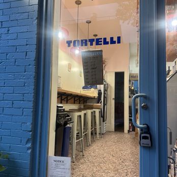 Tortelli - Inside Tortelli in Brooklyn, NY, visible through a glass door, with seating, a menu, and interior lighting. - Italian Near Me - Brooklyn, New York
