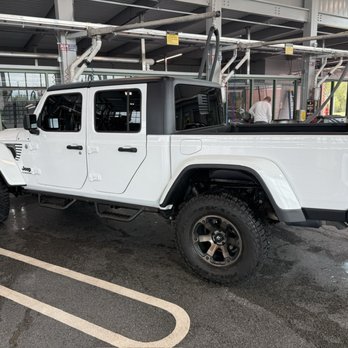 Drive & Shine - A white Jeep pickup truck with black accents is parked inside a vehicle service area, with a black roof and large off-road tires. - Car Wash Near Me - Crown Point, Indiana