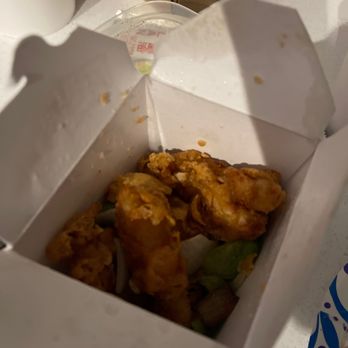 New Dragon - Burnt Sweet And Sour Chicken - A white cardboard takeout box with fried chicken pieces inside is open on a table. The chicken appears crispy and golden-brown. The table also has a plastic cup, a paper plate, and a cardboard food container nearby. The image is taken from above, showing the interior of the box and some surrounding items. - Chinese Near Me - Albuquerque, New Mexico