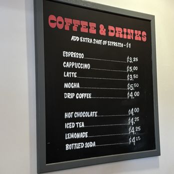 Churn - A black framed chalkboard menu lists various coffee and drink options with prices, including espresso, cappuccino, latte, mocha, drip coffee, hot chocolate, iced tea, lemonade, and bottled soda. The menu features a note about adding an extra shot of espresso for $1. The prices range from $3.25 to $5.50. The board is mounted on a white wall, and the text is written in white and pink chalk or marker. - Ice Cream & Frozen Yogurt Near Me - Phoenix, Arizona