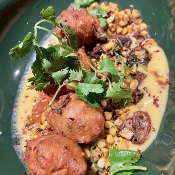 Lynette - Three fried food balls are arranged on a green plate, garnished with fresh cilantro. They are served with a side of corn and sautéed vegetables, including mushrooms and greens, in a yellow sauce. The dish appears to be a savory appetizer or entrée with a variety of textures and flavors. - Beer Bar Near Me - Minneapolis, Minnesota