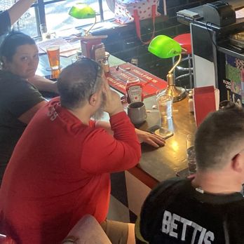 Retro Burger - Bar area - Four individuals sit at a bar counter inside a restaurant, with drinks, condiments, and green lamps on the counter, and a window in the background. - Gastropubs Near Me - Bethlehem, Pennsylvania