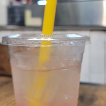 Simply Boba - Lemonade with dragon fruit boba - A clear plastic cup contains lemonade with dragon fruit boba, a yellow straw, and is placed on a wooden table in a cafe setting. - Bubble Tea Near Me - Lancaster, New York