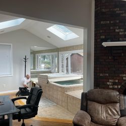 J Serino Inspections - An interior view of a room with a hot tub and a brick fireplace, where a home inspector kneels to examine an outlet.