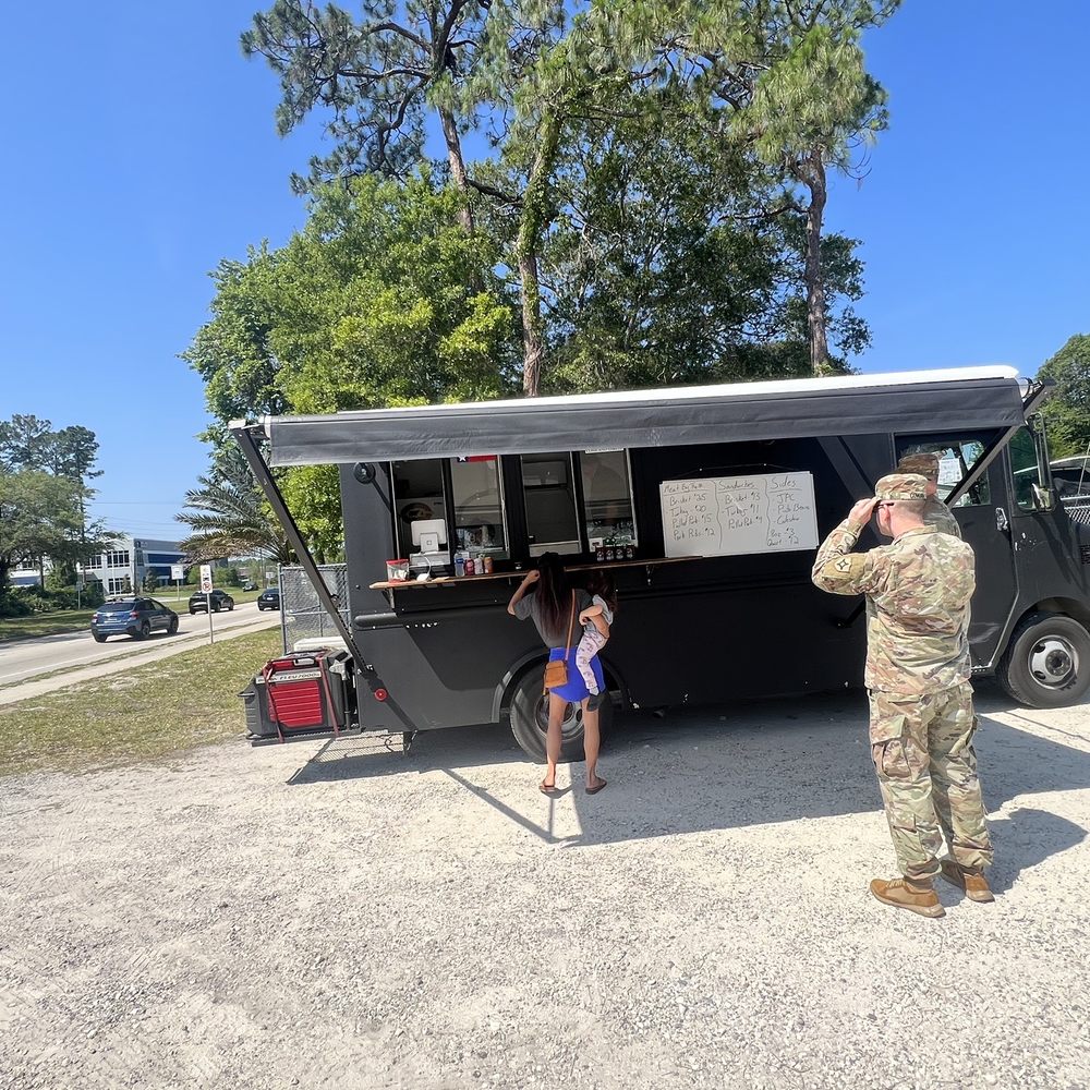a soldier taking a picture of a little girl standing in front of a food truck a soldier taking a picture of a little girl standing in front of a food truck