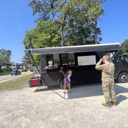 a soldier taking a picture of a little girl standing in front of a food truck a soldier taking a picture of a little girl standing in front of a food truck