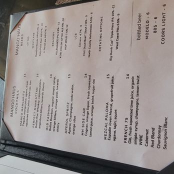 Mango Haus Lounge  - A menu from Mango Haus Lounge is displayed on a table, with a textured placemat partially visible. The menu lists various drinks and food items. - New American Near Me - Tehachapi, California