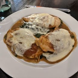 Chicken Saltimbocca - A dish of chicken saltimbocca topped with melted cheese and served with a sauce, on a white plate at a restaurant.