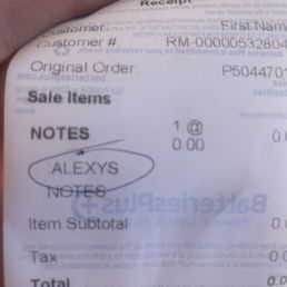 The image shows a receipt from Batteries Plus in Avondale, AZ, with details including customer name, customer number, order number, and sale items. The receipt notes a purchase for 'ALEXYS' with a quantity of one. The receipt includes sections for subtotal, tax, total, and sale amount received, with some text partially obscured by a person's hand holding the receipt. The background appears to be a plain surface.