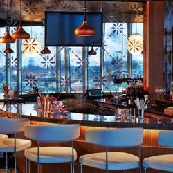 VASO - Chic indoor bar at VASO with modern pendant lighting, backlit shelves, and floral-patterned glass framing the city beyond.