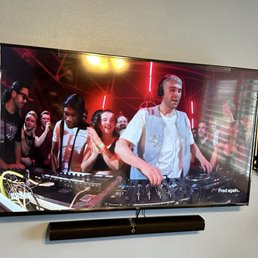 Tv Mounting, sound bar - A DJ is seen mixing music at a party, with a crowd of people dancing and smiling in the background, illuminated by colorful lights.