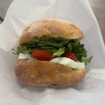 Method Cafe - A sandwich featuring a crusty bread roll filled with cherry tomatoes, leafy greens, and slices of mozzarella cheese. - Coffee & Tea Near Me - Newark, New Jersey