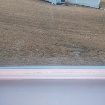 Squeegee Squad - Window frame itself left with drips on white plastic and sticky drips on the handle you use to open - A window with visible drips on the white plastic frame and sticky residue on the handle, overlooking a brown grassy yard with a house in the background. - Window Washing Near Me