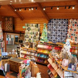 The Quilter's Lodge - More quilts on display hanging above the shelves of colorful fabric.