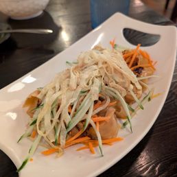 Fried Pork Dumplings - Dumplings with shredded cucumber, carrots, and crispy strips are served on a white dish at a restaurant table.