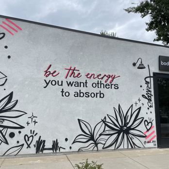 Bodied - A mural on an exterior wall features a motivational quote, floral illustrations, and decorative elements in black, white, and pink, with a door and signage nearby. - Pilates Near Me - Denver, Colorado
