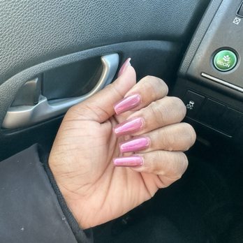 Nail Spa - This is supposed to be a pink cat eye. I just don't see it - The image depicts a hand with long, pink, glossy acrylic nails, positioned near the interior door handle of a car. The person is wearing a dark jacket, and the background includes part of the car's dashboard and door panel, with a green ECON button visible. - Nail Salons Near Me - Towson, Maryland