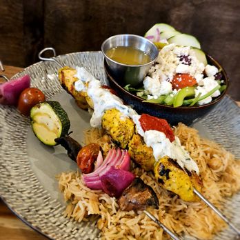 Oso - A dish featuring grilled kebabs served over rice, accompanied by vegetables and a side salad with cucumbers, tomatoes, and feta cheese. - Spanish Near Me - Silverton, Oregon