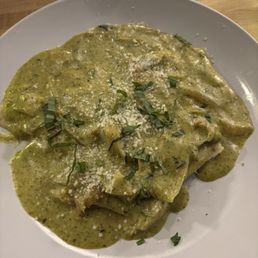 Artichoke Ravioli Giardino - Artichoke ravioli covered in a green sauce, topped with grated cheese and chopped herbs, served on a white plate.