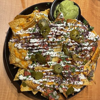 Lavender Grill - Lavender Nachos - A plate of nachos with cheese, jalapeños, sour cream, and chopped vegetables, served with guacamole on the side. - Steakhouses Near Me - Ottawa, Ontario