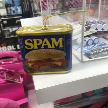 Five Below - Because your Christmas tree wouldn't be complete without it. - A can of SPAM Classic, featuring a label with an image of a sandwich, is placed on a white store counter. The can has a gold-colored lid with a string attached, possibly for display or decorative purposes. In the background, there are shelves with various products, including batteries and other small items, and a clear plastic display case. The setting appears to be a retail store or convenience shop. - Toy Stores Near Me - Gaithersburg, Maryland