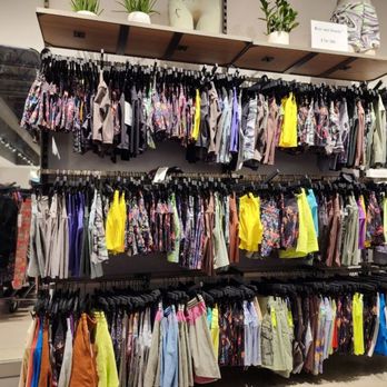 Lululemon - Multiple clothing racks display men's shorts and swimwear in different colors, patterns, and sizes. The store has a neutral interior with shelves above the racks holding potted plants and decorative items. The image shows a retail environment focused on casual and athletic apparel. - Sports Wear Near Me - Rosemont, Illinois