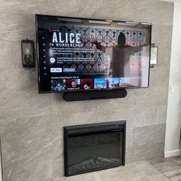 Perfectly mounted 65-inch tv between two wall lights and above an electric fireplace