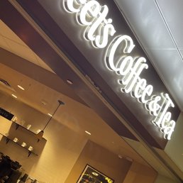 the entrance to a coffee shop - The image shows an illuminated sign with the text "Peet's Coffee & Tea" inside a coffee shop, with part of the interior visible.