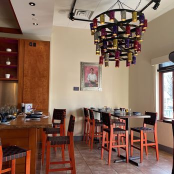Rosa Mexicano - a dining room with a bar and chairs - The image shows a restaurant interior with a multicolored chandelier hanging from the ceiling, wooden chairs with dark cushions, and a framed portrait on the wall. - Mexican Near Me - Hackensack, New Jersey