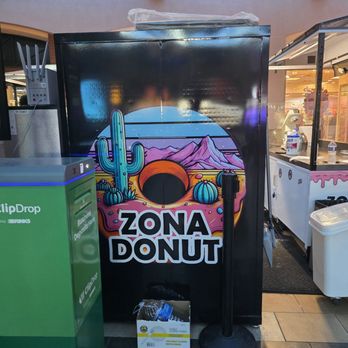 Zona Donut - A black kiosk features a vibrant desert-themed logo for Zona Donut, with cacti, mountains, and a sunset, located inside a shopping mall. - Donuts Near Me - Tucson, Arizona