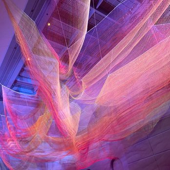 Renwick Gallery - A large, colorful fabric sculpture with pink, orange, and purple hues hangs from the ceiling of a modern building interior. - Art Galleries Near Me - Washington, DC, District of Columbia