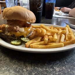 Cheese Curd Burger - A cheeseburger with cheese curds, pickles, and a bun is served with French fries on a white plate at a restaurant.