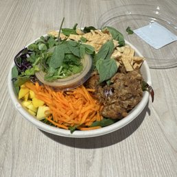 Satay Bowl - A satay bowl containing shredded carrots, chopped yellow vegetables, fresh herbs, and fried protein pieces, served on a wooden table.